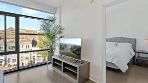 Une chambre moderne avec une grande fenêtre, un téléviseur posé sur une étagère intégrée, un lit et une plante en pot.
