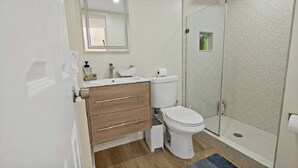 A modern bathroom with a wooden vanity, white sink, toilet, and a glass shower enclosure. - Warm and Bright Home | Metro | 1 Min Walk | Md (Capitol Heights)