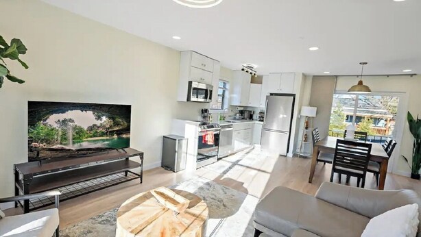 A modern kitchen with white cabinets, a built-in oven, and a refrigerator. There is a dining area with a table and chairs, and a large window providing a view of the outdoors. - Warm and Bright Home | Metro | 1 Min Walk | Md (Capitol Heights)