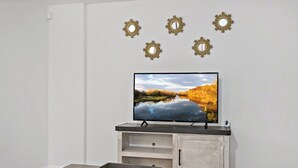 A living room with a flat-screen TV on a wooden stand, a coffee table, and a wall-mounted TV stand with decorative sunburst mirrors. - Private Capitol Heights Guest Suite near Metro with Laundry (Capitol Heights)