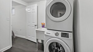 A laundry room with a stacked washer and dryer, a small sink, and a door leading to another room. - Private Capitol Heights Guest Suite near Metro with Laundry (Capitol Heights)