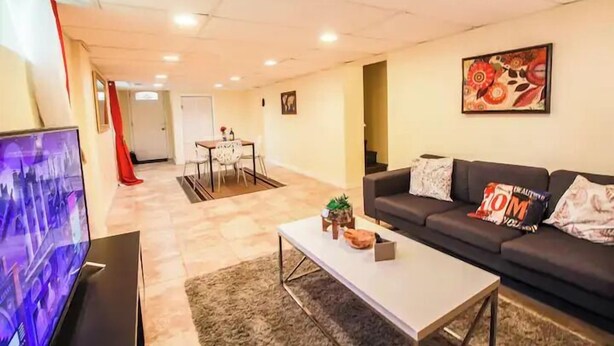 A living room with a sofa, coffee table, TV, and a painting on the wall. - Arlington | Lower Suite | Center | Efficiency (Arlington)