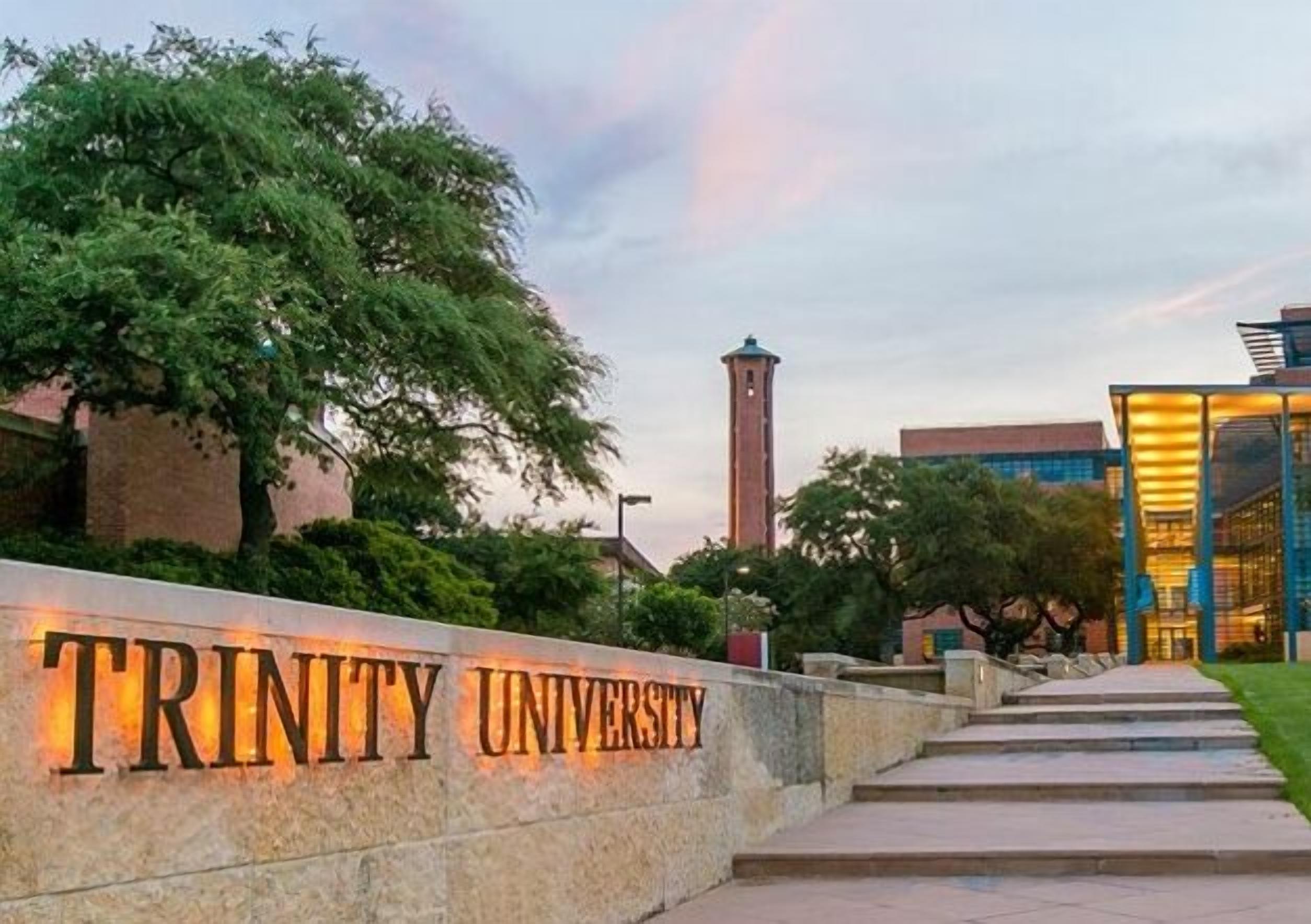Der Eingang zur Trinity University mit einem markanten Schild, einem Weg zum Gebäude und einem Turm im Hintergrund.
