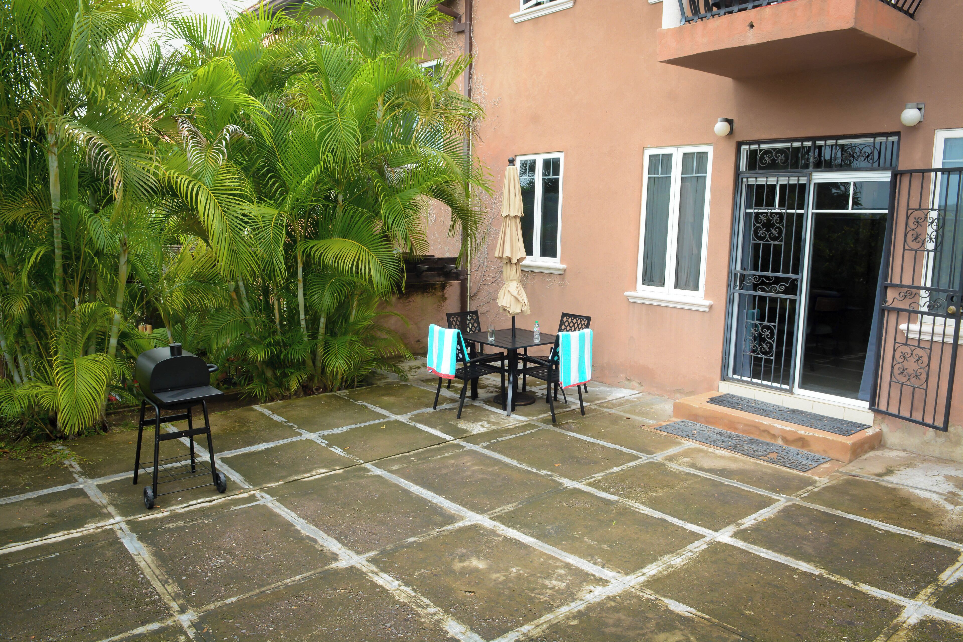Une terrasse équipée d’un barbecue, d’une table, de chaises et d’un petit jardin agrémenté de palmiers.
