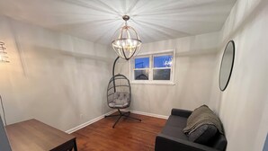 Une pièce avec un plancher en bois, un canapé noir, un fauteuil suspendu, une table à manger et une fenêtre donnant sur un pont.