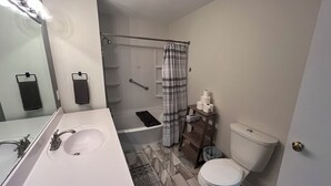 Une salle de bain avec un lavabo blanc, un miroir, une douche, des toilettes et un tapis à motifs.