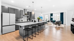 A modern kitchen with a central island, bar stools, and a dining area with a sofa and curtains.