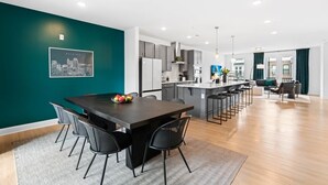 A modern kitchen with grey cabinets, a central island, and a dining area with a dark table and chairs.