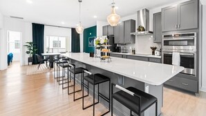 A modern kitchen with a large island, bar stools, stainless steel appliances, and pendant lighting.