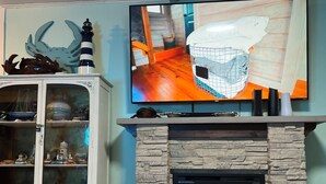 Una sala de estar con chimenea de piedra, un televisor montado encima y un aparador con puertas de cristal que exhibe varios objetos.