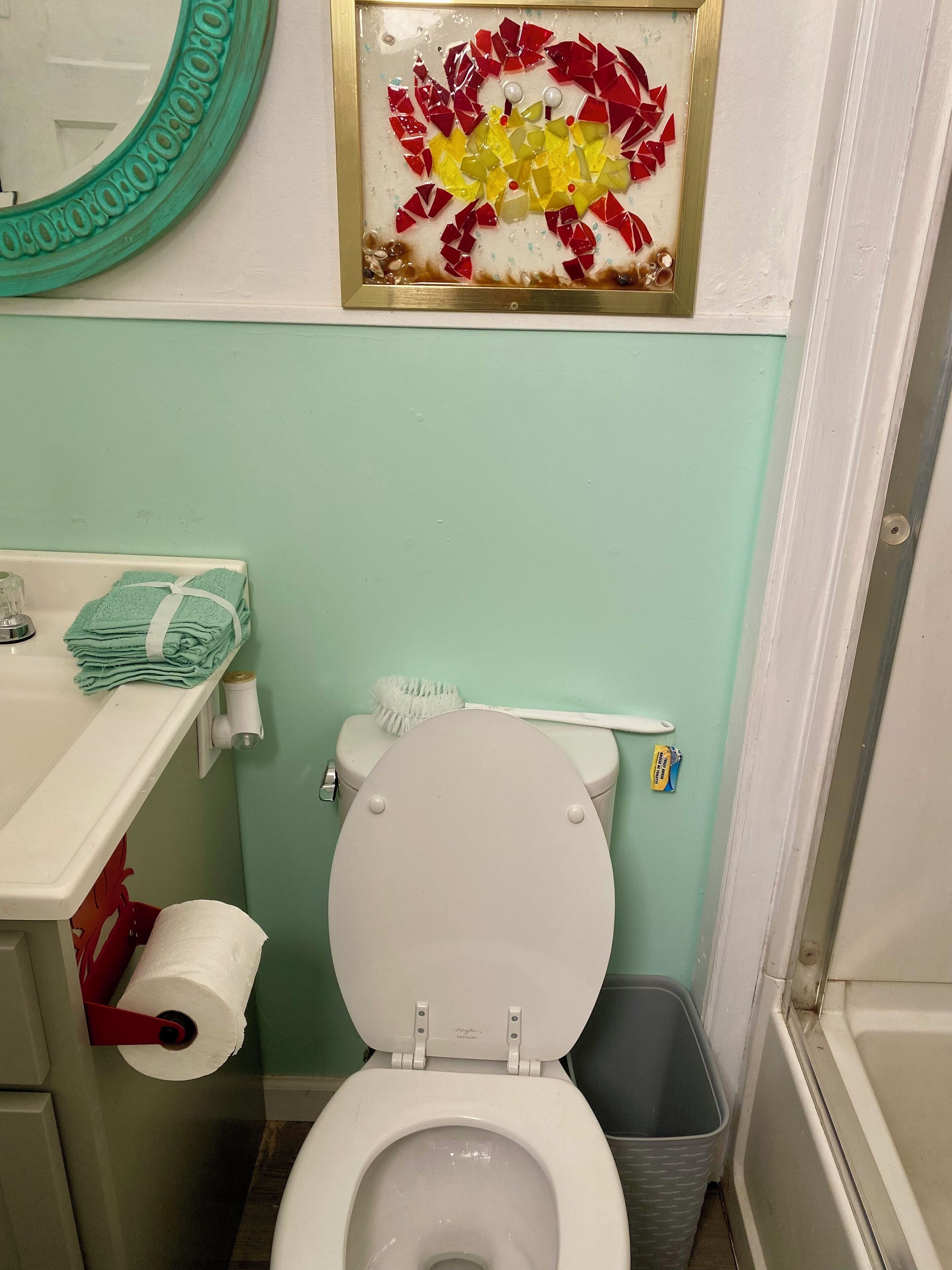 Un baño con inodoro, lavamanos, dispensador de papel higiénico, cepillo de dientes y un cubo de basura.