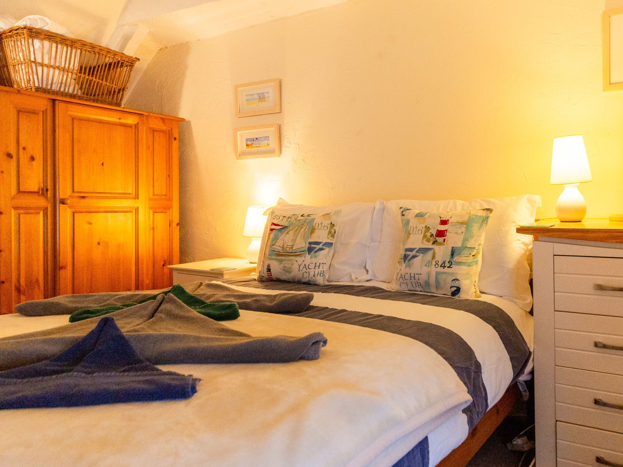 Une chambre à coucher comprenant un lit, une armoire en bois, une table de chevet, une lampe et un mur orné de tableaux encadrés.
