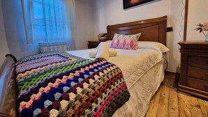 Un lit avec une couverture colorée, une tête de lit en bois, une table de chevet avec une lampe et un tableau accroché au mur.