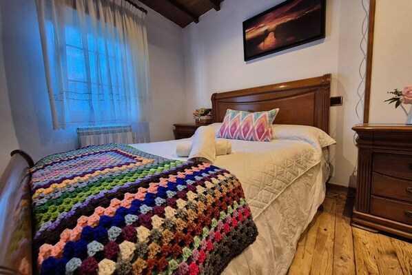 A bed with a colorful blanket, a wooden headboard, a bedside table with a lamp, and a painting on the wall. - 38A01 Casa El Canton (Riosa)