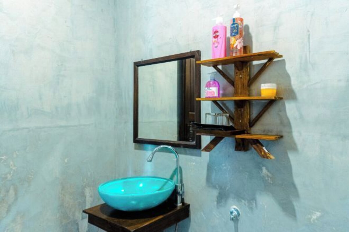 A bathroom with a turquoise sink, a wooden shelf with toiletries, and a mirror with an open frame.