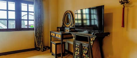 A room with a TV, a decorative cabinet, a small table, and a window with curtains.