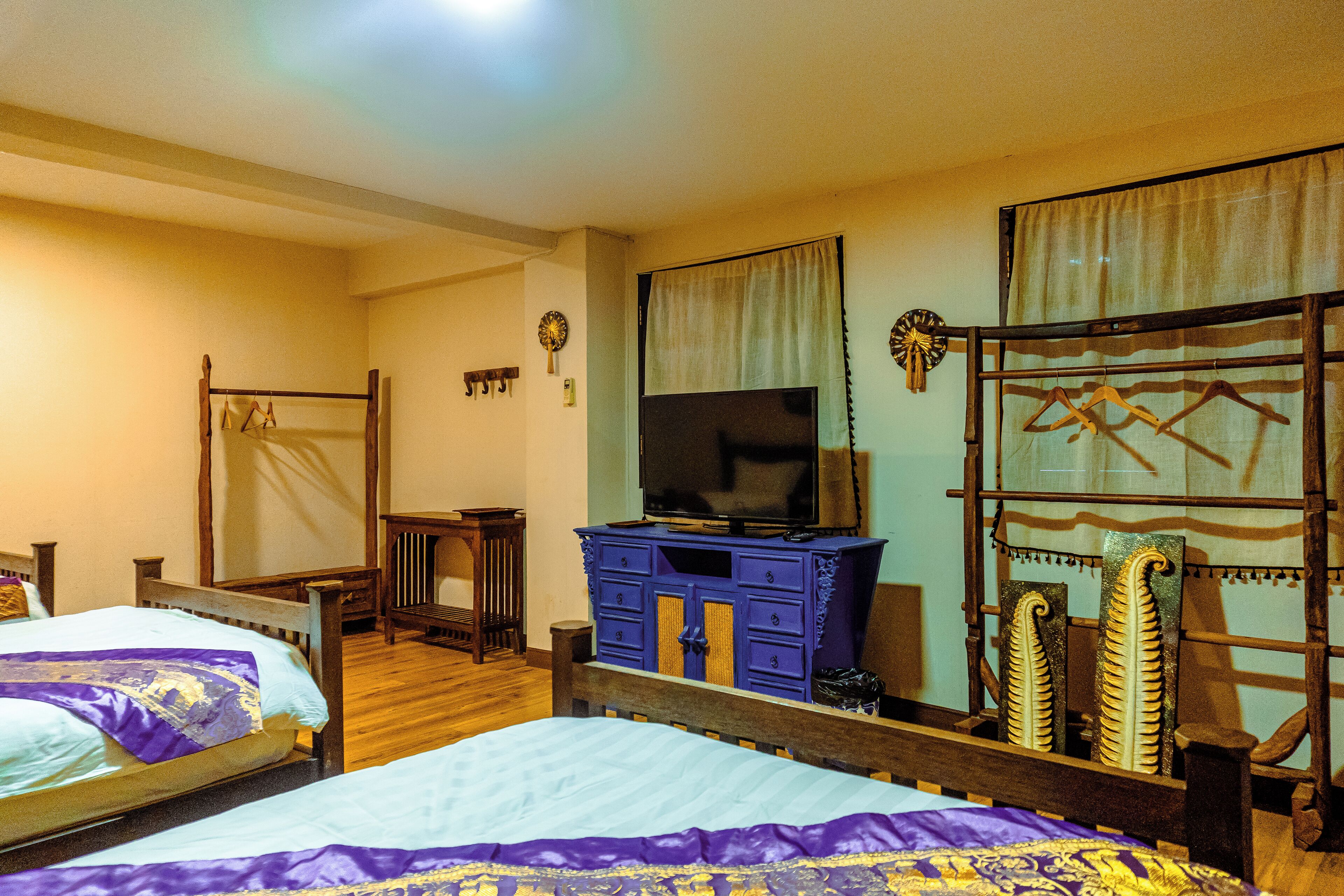 A bedroom with two beds, a TV on a dresser, and a mirror with a curtain.