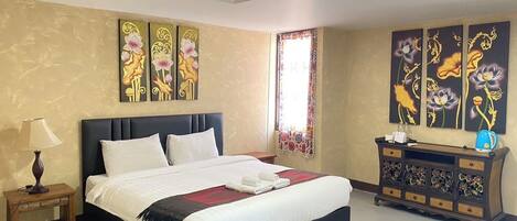 A hotel room with a large bed, a nightstand, a dresser with decorative items, and floral artwork on the walls.
