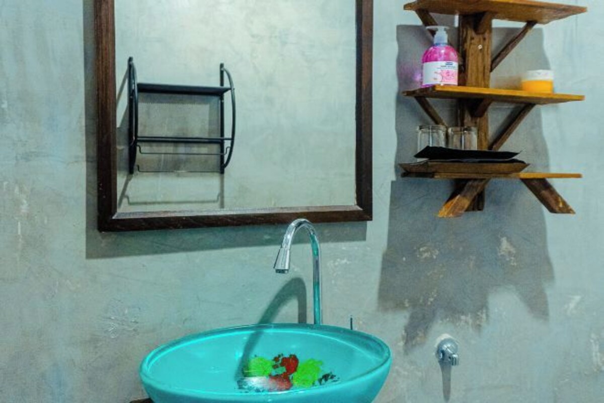 A bathroom with a glass sink, a mirror, and wooden shelves holding toiletries.