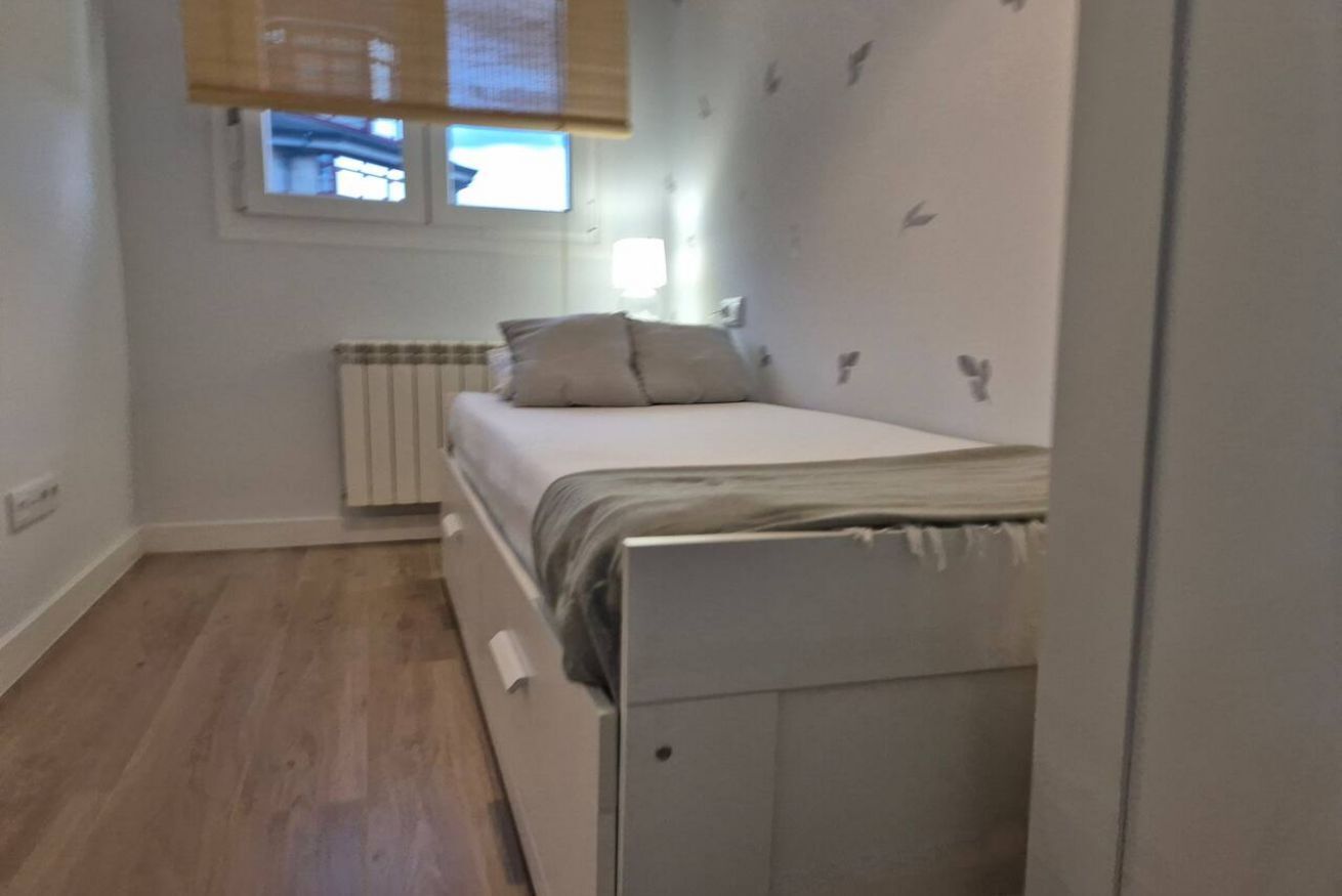 Une petite chambre avec un lit simple, un radiateur, une fenêtre avec des stores et une étagère fixée au mur.
