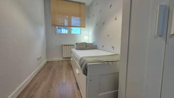 Un dormitorio pequeño con cama, un radiador, una ventana con persianas y una puerta.