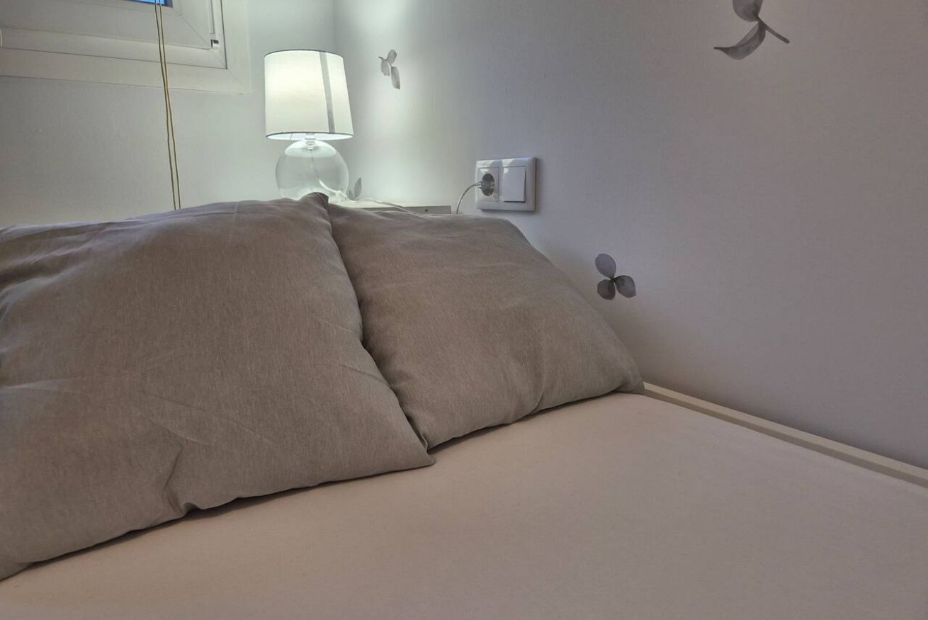 A bed with a beige blanket, a bedside lamp, and wall-mounted light switch.