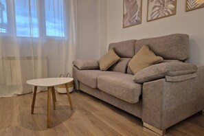 A living room with a sofa, a small round table, and a window with sheer curtains. - 650A Apartamento moderno, acogedor y con garaje (Oviedo)