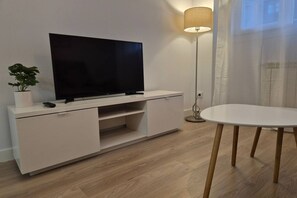 A modern living room with a flat-screen TV on a white cabinet, a small table, a floor lamp, and a potted plant. - 650A Apartamento moderno, acogedor y con garaje (Oviedo)