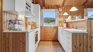 A compact kitchen with wooden walls, white cabinets, a window with curtains, and hanging pendant lights.