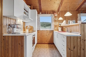 A compact kitchen with wooden walls, white cabinets, a window, and pendant lights.