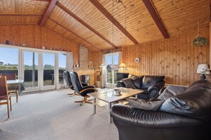 A wooden interior with a leather sofa, a dining table, and a fireplace.