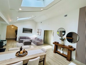 A spacious living area with a high ceiling, a sectional sofa, a dining table with chairs, and a skylight. - Relaxing 3BD 2BA Home in Walnut Creek with a Fireplace, HotTub, & More. (Walnut Creek)