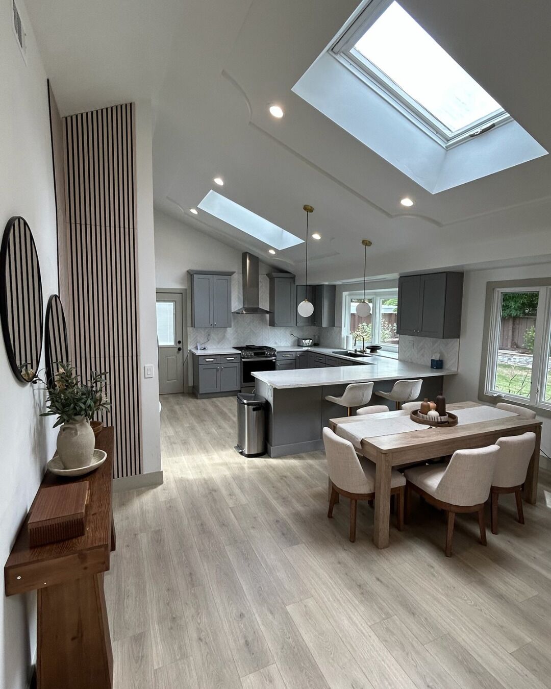 A modern kitchen with a skylight, a dining area with a wooden table and chairs, and a large island with a sink.