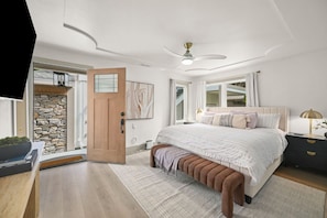 A bedroom with a bed, bedside tables, a bench, a ceiling fan, and a door leading to a balcony.
