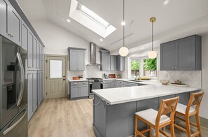 A modern kitchen with grey cabinets, a central island, wooden chairs, and a skylight.