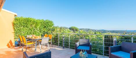Une terrasse meublée de mobilier en osier, avec une table et des chaises, donnant sur un paysage verdoyant luxuriant.