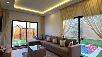 A modern living room with a sectional sofa, a coffee table, and a view of a backyard with a swimming pool.