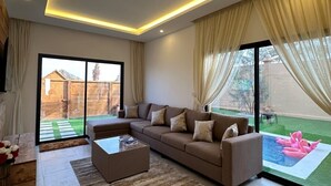 Uma sala de estar moderna com sofá seccional, uma mesa de centro e vista para um quintal com piscina.