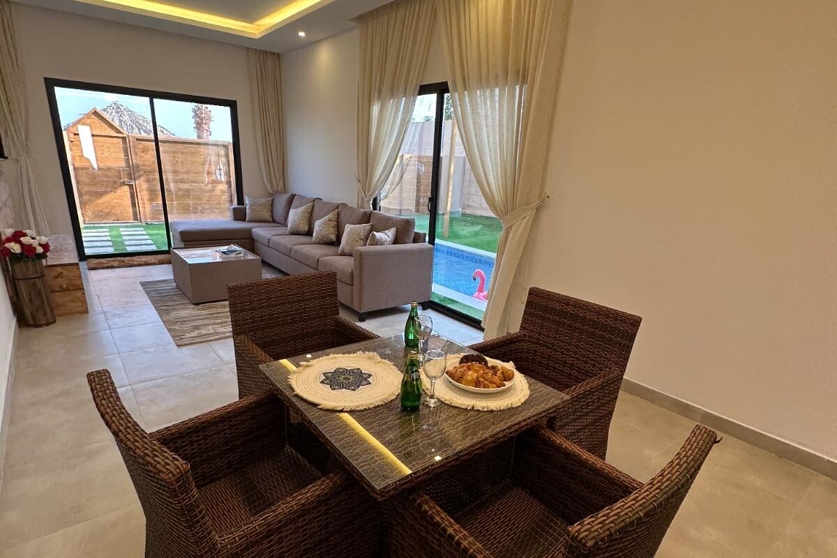 A modern living room with a dining area, wicker furniture, and a view of a swimming pool.