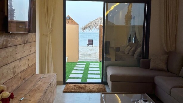 Uma sala de estar moderna com uma grande porta de vidro deslizante que dá para a praia, um sofá, uma mesa de centro e um painel de parede de madeira.