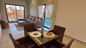 Uma sala de estar moderna com área de jantar, móveis de vime e vista para uma piscina.