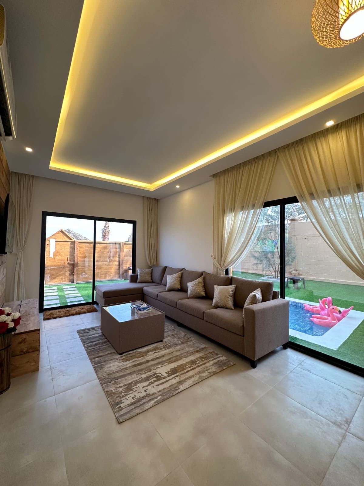 A modern living room with a sectional sofa, a coffee table, and a view of a backyard with a swimming pool.