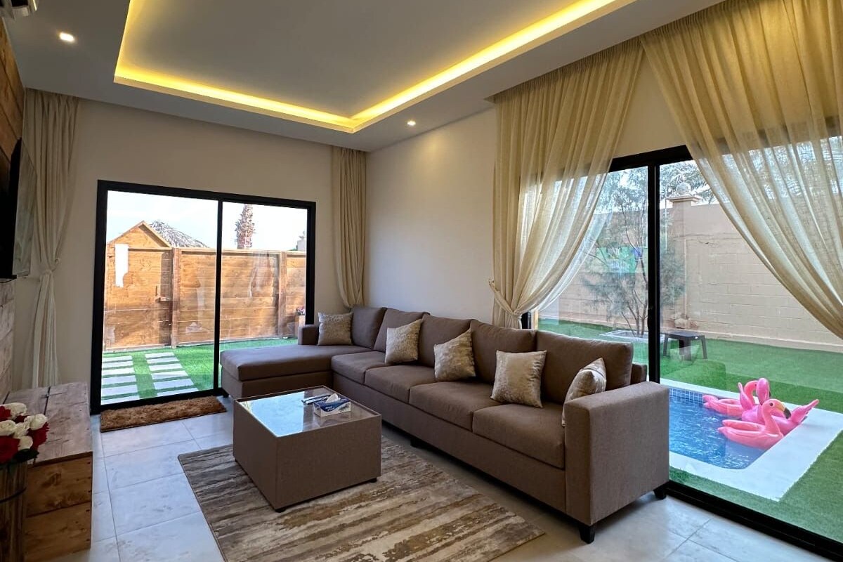 A modern living room with a sectional sofa, a coffee table, and a view of a backyard with a swimming pool.