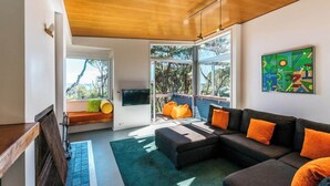 Un salon moderne avec un canapé d’angle, une grande fenêtre et une vue sur l’extérieur.