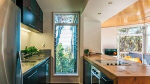 Une cuisine moderne avec des meubles de couleur sombre, un plan de travail en bois et une grande fenêtre offrant une vue sur les arbres.