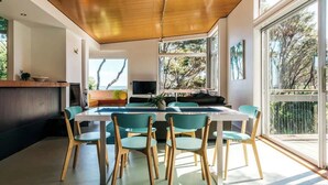 Un espace repas moderne avec un plafond en bois, de grandes fenêtres et une vue sur l’extérieur.