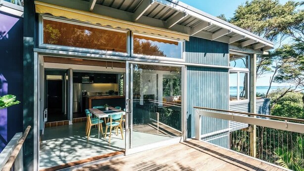 Une maison moderne dotée d’une terrasse, de grandes portes vitrées et offrant une vue sur l’océan.