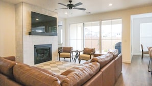 A living room with a fireplace, leather sofas, a flat-screen TV, and a ceiling fan.