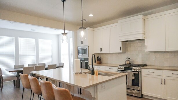 A modern kitchen with white cabinets, a central island with bar stools, stainless steel appliances, and pendant lighting.