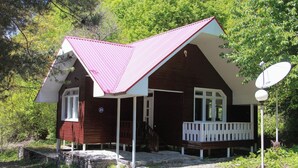 Une cabane en bois avec un toit rouge, des boiseries blanches et une véranda dotée d’une balustrade blanche.